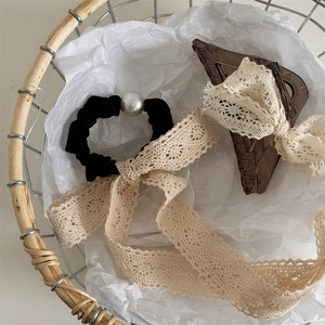 Detail of beige lace bow claw clip and pearl ribbon scrunchie in a woven basket