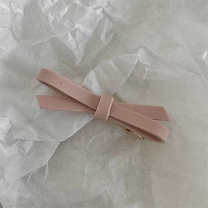 Detail of pink suede bow hair clip with golden metal fastener on textured paper