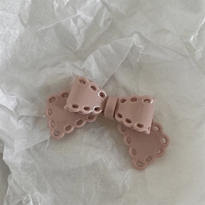 Close-up of pink cream bow hair clip with decorative cut-out edges on white paper
