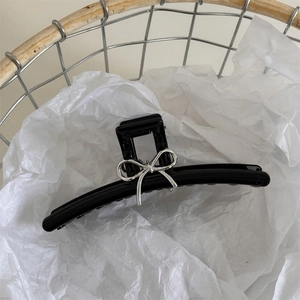 Dettaglio di una pinza per capelli nera lucida con fiocco in metallo argento su carta bianca
