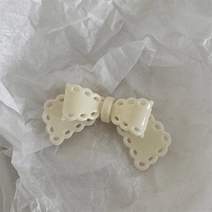 Detail showing cream-colored scalloped edge bow hair clip on textured paper background