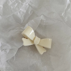 Detailed view of a creamy white resin bow hair clip with a golden metal duckbill base