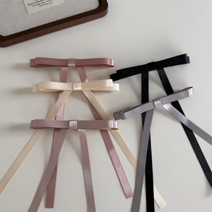 Detail view showing assorted colors of long ribbon bow hair clips on a minimalist background