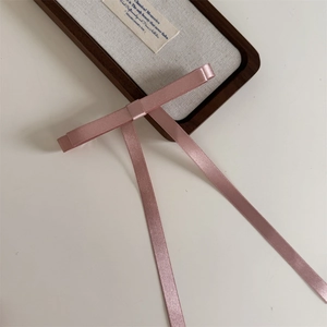 Detail of pink satin bow hair clip with long ribbons on a decorative wooden tray
