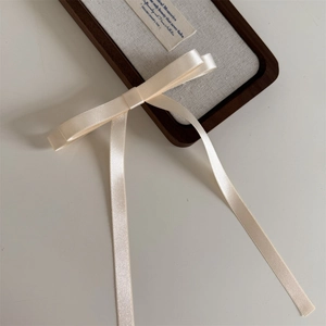 Close-up of cream satin bow hair clip with long flowing ribbons and elegant layered silk