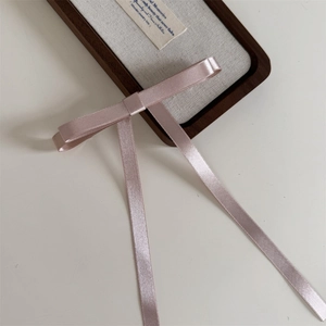 Detail of soft pink satin bow hair clip with long ribbons on a wooden tray