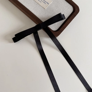 Detail of elegant black long ribbon bow hair clip on a walnut wood jewelry display tray