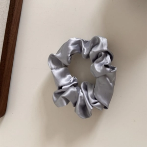 Close-up of elegant silver grey satin scrunchie with soft silk texture and pleated detail