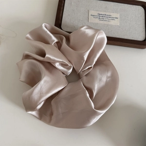 Close-up of elegant champagne satin oversized scrunchie with high gloss and elastic texture