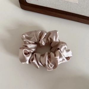 Detail of soft champagne satin scrunchie with elegant folds and silky texture