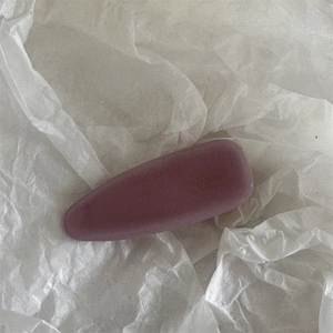 Détail d'une pince à cheveux en acétate rose poudré mat sur fond de papier froissé