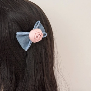Detailed view of denim bow hair clip with pink fabric rose worn on black hair
