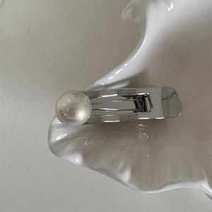 Détail de pince à cheveux argentée avec perle lumineuse sur plateau coquillage