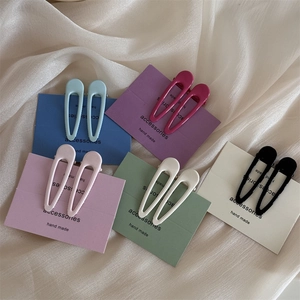 Dettaglio di fermagli per capelli a goccia color pastello su seta beige con confezione