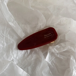 Détail macro d'une barrette en acétate rouge foncé avec inscription dorée élégante