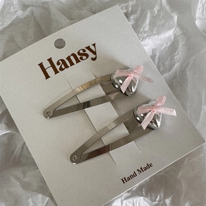 Close-up of two silver heart hair clips with pink bows on a display card packaging