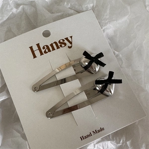 Close-up of two silver heart hair clips with black bows on a white display card