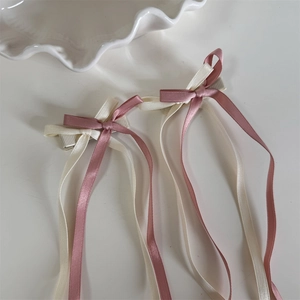 Detail von Haarklammern mit langen Satinschleifen in Rosa und Creme auf Weiß