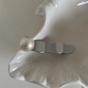 Détail d'une pince à cheveux argentée ondulée avec perle sur un plateau en céramique