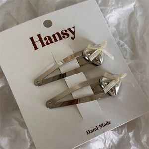 Detail view of silver heart hair clips with cream ribbon bows on brand display card