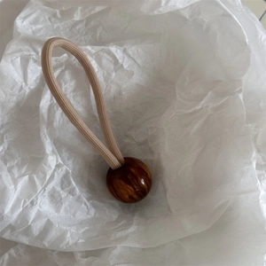 Détail d'un élastique à cheveux beige avec perle ambrée marbrée sur papier froissé
