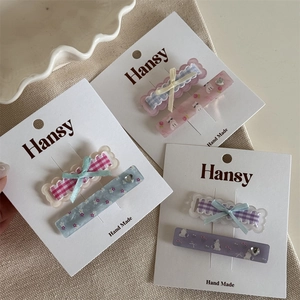 Close-up of pastel plaid bow hair clips and floral resin slides on canvas texture