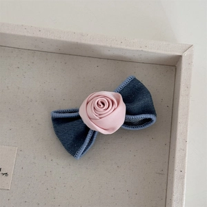Detailed close-up of blue denim bow and pink satin rose hair clip showing fabric texture