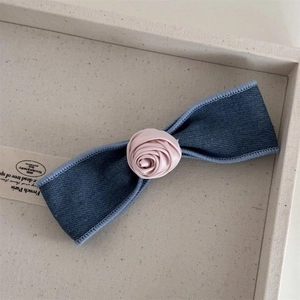 Detail of denim bow hair clip with a pink satin rose on a jewelry tray backdrop