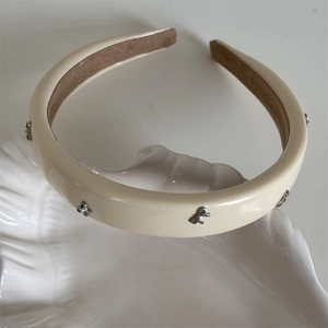 Détail du serre-tête en cuir crème orné de petits nœuds métalliques argentés