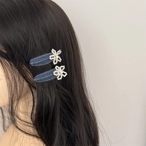 Close-up of a pair of dark denim hair clips with white faux pearl flower decorations