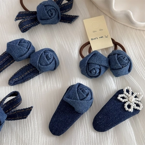 Detail view of denim rose hair clip and tie with yellow stitching and pearl accents