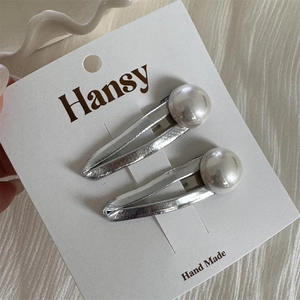 Détails des barrettes argentées texturées avec perles blanches sur carte Hansy