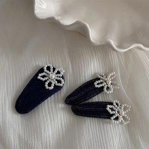 Detail view of denim hair clip set with pearl flowers and yellow stitching