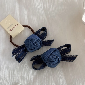 Detail of blue denim rose hair ties with orange stitching on soft white fabric background