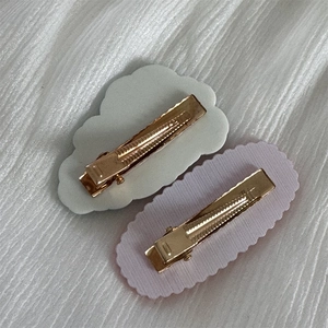 Detail view of gold metal alligator hair clips with white cloud and purple oval plates