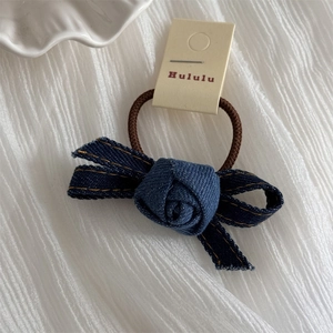 Detail view of handmade denim rose hair tie with orange stitching and brown elastic