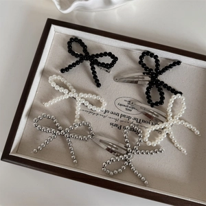 Detailed view of handmade beaded bow hair clips with pearls and metallic beads in a tray