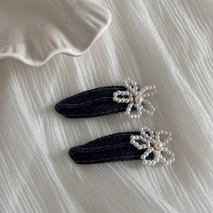 Macro detail of dark denim fabric hair clips with small pearl flower and orange stitching