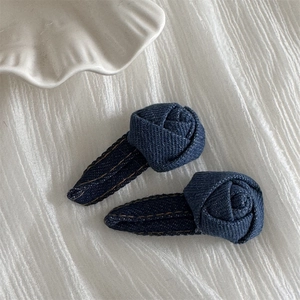 Detail of two dark blue denim rose hair clips on white textured fabric background
