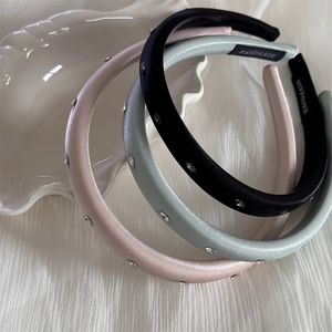 Détail de trois serre-têtes en satin noir, menthe et rose ornés de strass brillants