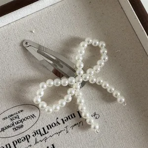 Detail view of a silver BB hair clip featuring a white faux pearl beaded bow on a tray