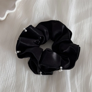 Gros plan du chouchou en satin noir avec perles blanches sur tissu blanc gaufré