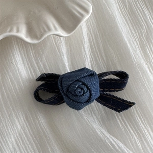 Detail shot of the dark blue denim rose flower hair clip on a textured white fabric background