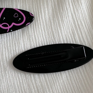 Detail view of oval hair clips with pink heart patterns and sturdy black metal duckbill clips