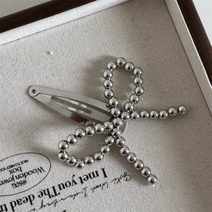 Macro view of silver beaded bow hair clip on a minimalist linen jewelry box display