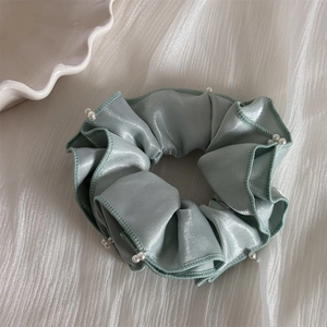 Détail du chouchou en satin vert menthe avec perles blanches pour coiffure élégante femme