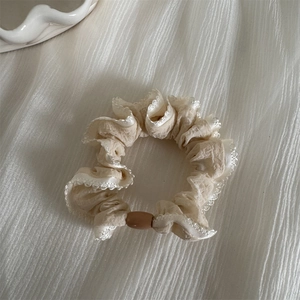 Detail of beige scrunchie with white lace edges and a brown bead on a white fabric surface