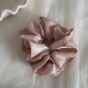 Détail d'un chouchou en satin rose orné d'élégantes perles blanches sur les bords