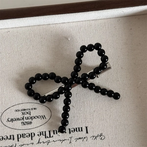 Close-up of black beaded bow hair clip with vintage duckbill metal clamp on canvas