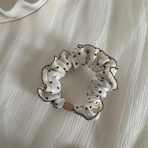 Close-up of cream polka dot scrunchie with scalloped black edges and a wooden ring buckle
